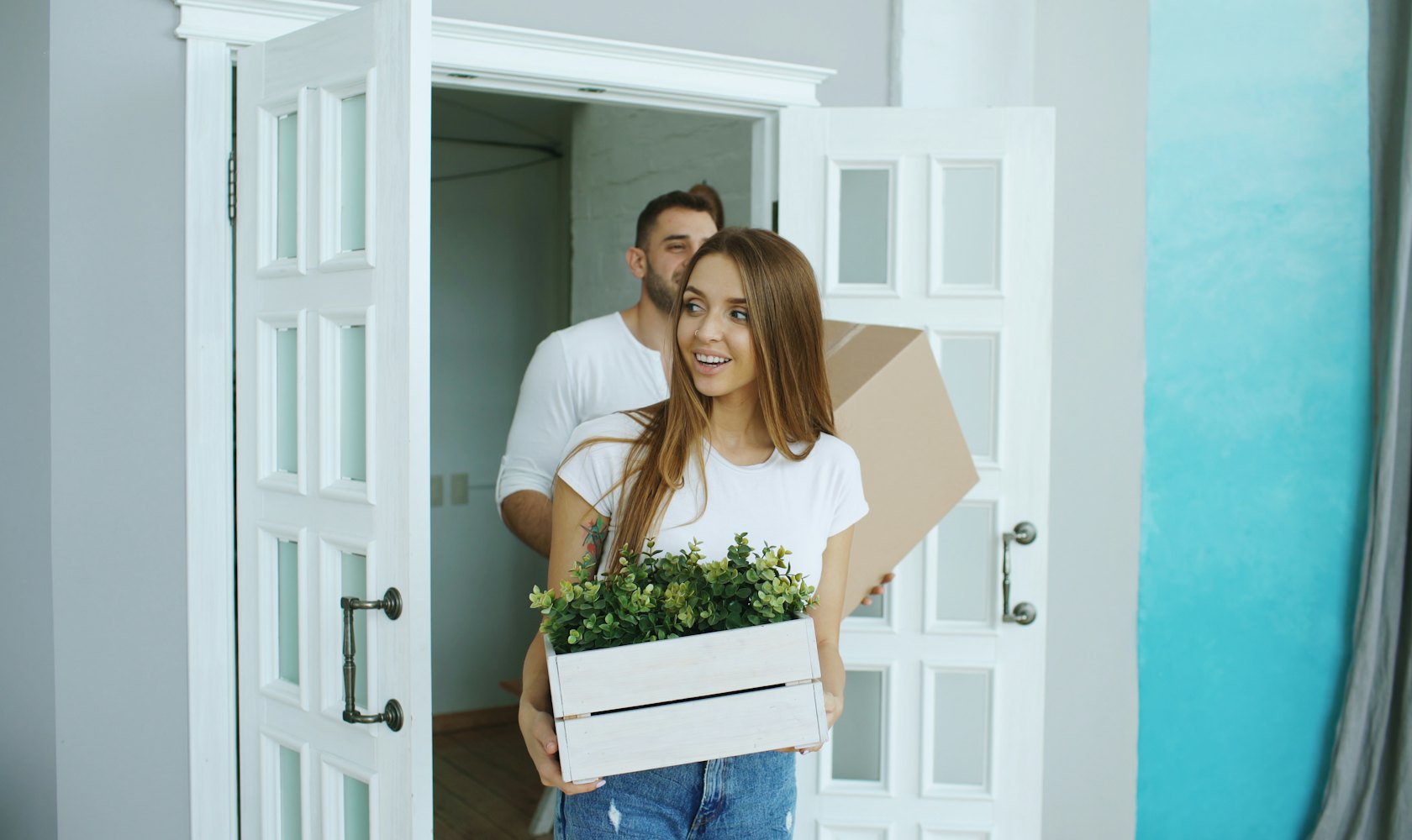A couple carrying a box and a plant into their bright new home